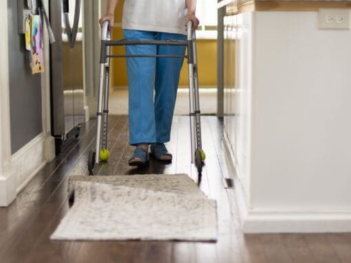 Person walking with walker approaches bunched rug.